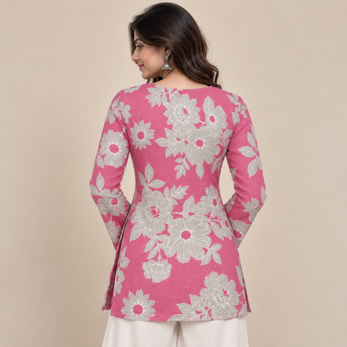 A woman shown from the back wearing a pink long-sleeve kurta with a large white floral pattern, paired with off-white trousers, against a solid beige background.