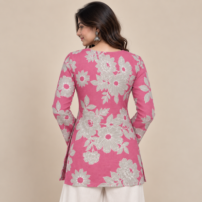 A woman shown from the back wearing a pink long-sleeve kurta with a large white floral pattern, paired with off-white trousers, against a solid beige background.
